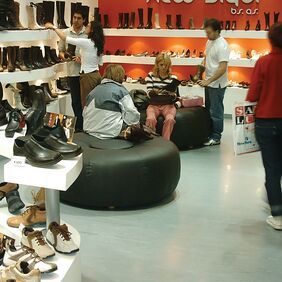 Green homogeneous flooring in a shoe retail shop with customers and seating 