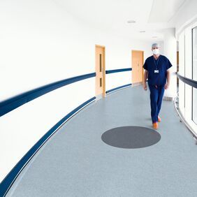 Blue safety flooring in a hospital corridor with a doctor walking 
