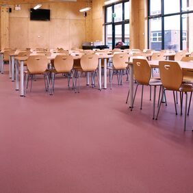Red colour safety flooring in a highschool canteen with chairs and tables 