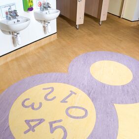 Light colour homogeneous flooring in a chidrens school toilet with a number motif design Incorporated