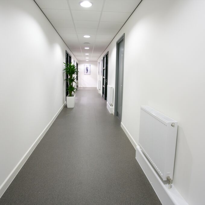 Grey stone effect safety flooring in a corridor with white walls and floor plants 