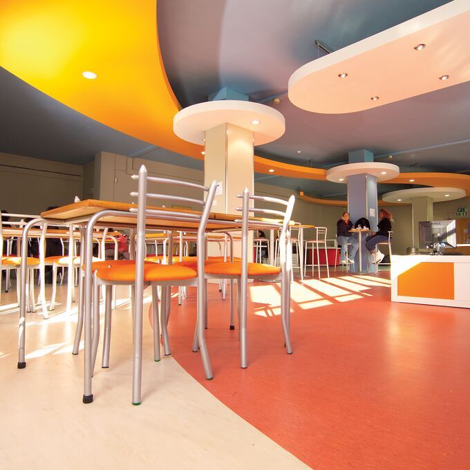 Rose coluor homogeneous flooring in a school canteen area with chairs and tables