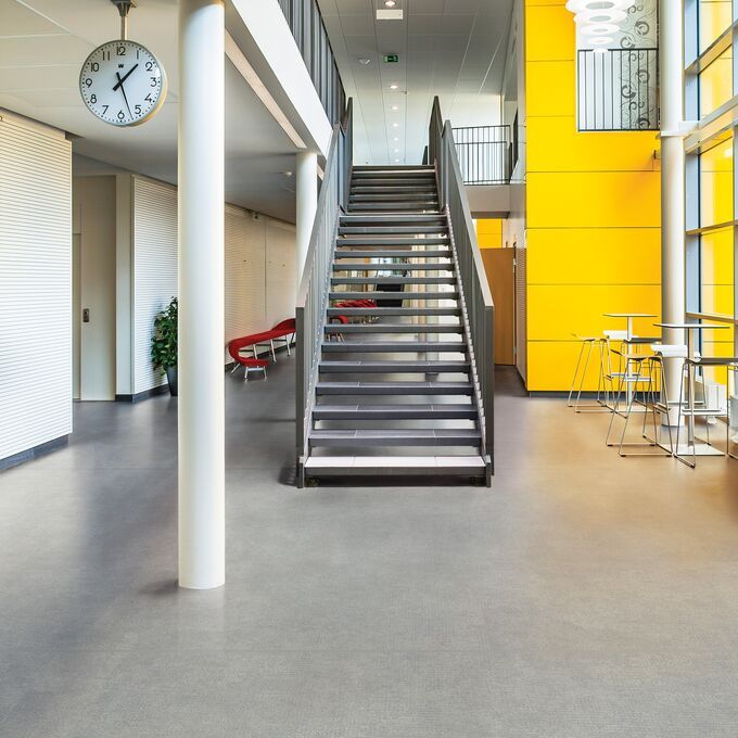 Light grey concrete effect safety flooring in a large corridor with a metal staircase and yellow panel walls